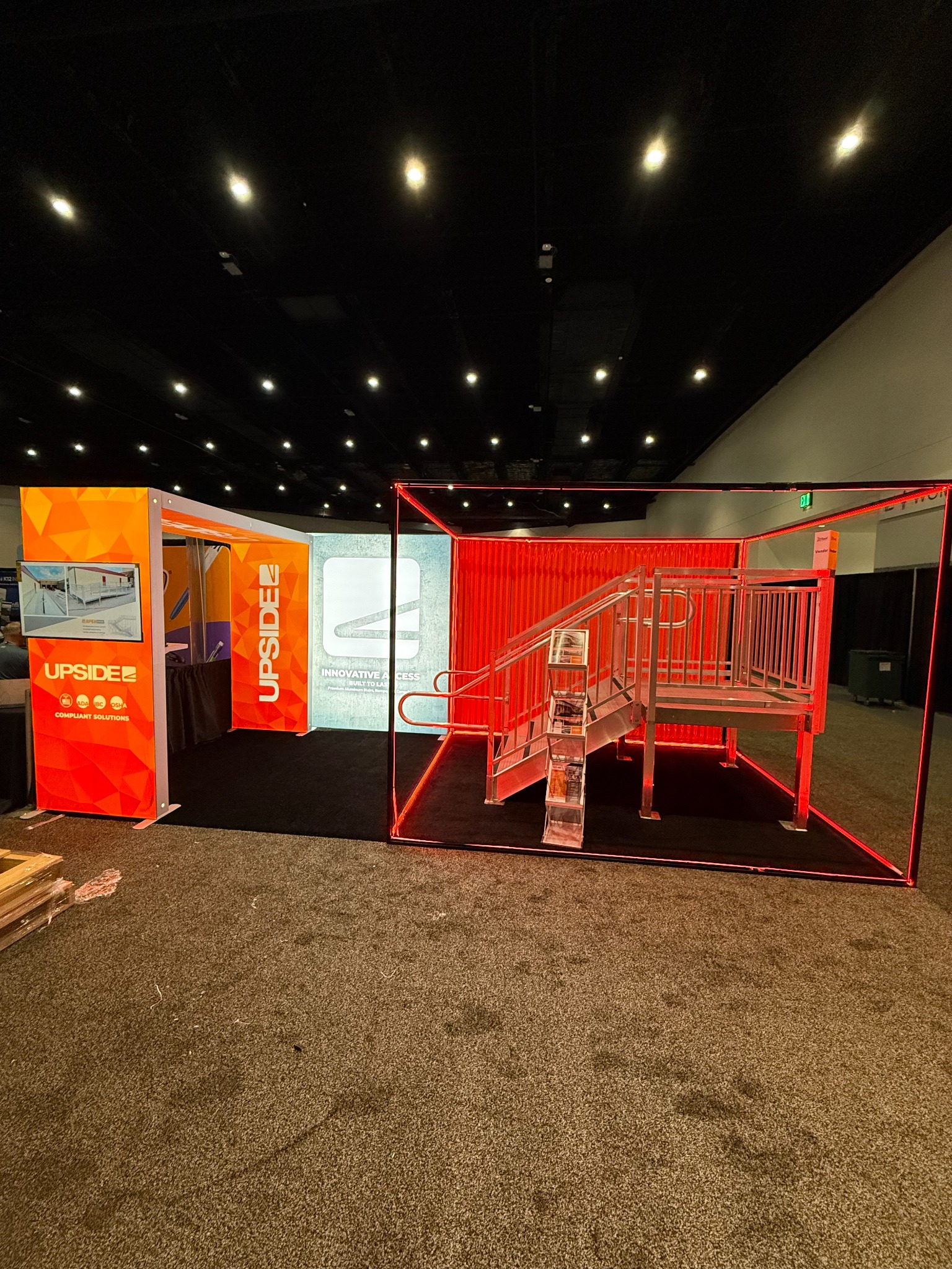 Upside Innovations trade show exhibit featuring an illuminated orange display and industrial access platform